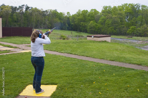 Woman at a clays shooting range using a shotgun to break targets. 
