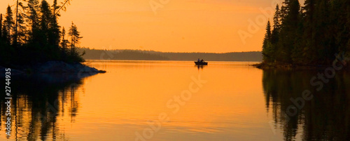fishing just before a colorful sunrise on a tranquil lake surrounded by thick forest