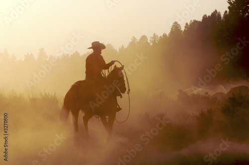 Silhouette of cowboy riding horse at sunset