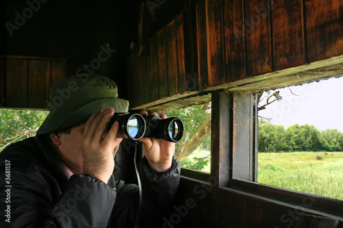 Man looking through binoculars in a birdwatching hideout