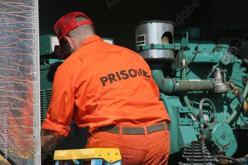 Prisoner repairing a vehicle. Working on some sort of engine.