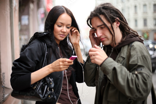 Young couple listening to a portable music player on a street