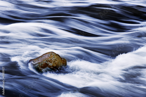 Water rushing by rock in river forming abstract appearance
