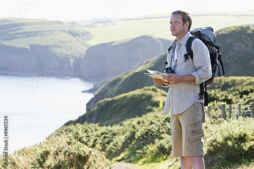 Man standing on cliffside path holding map