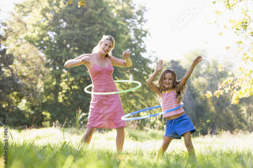 Woman and young girl outdoors using hula hoops and smiling