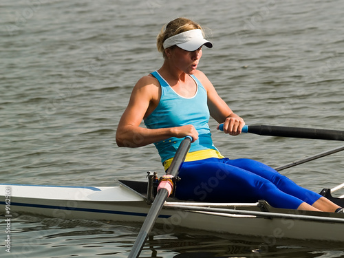 Sporty young lady rowing in boat on water