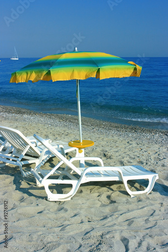 Colorful parasol over two chaise-longues on a beach