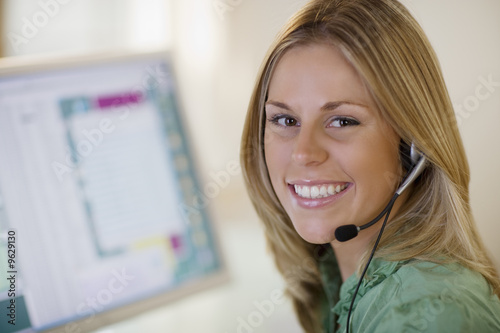 Smiling woman with headset and computer monitor