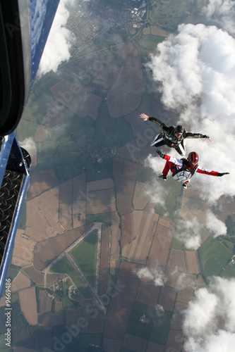 Two skydivers exit a plane in a sit position
