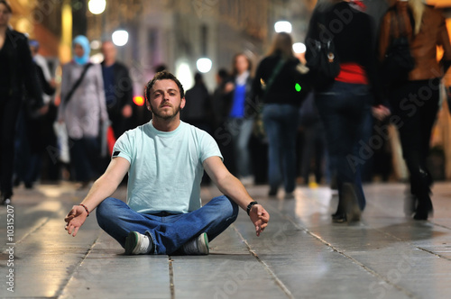 young man meditating yoga in lotus position at street