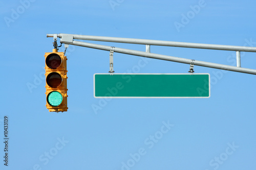 Green traffic signal light with sign on blue sky