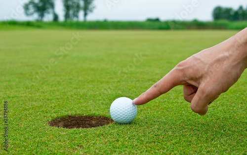 Man's hand pushing golf ball into the hole