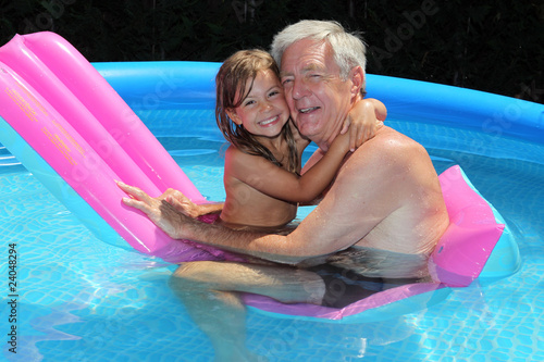 Grandfather and granddaughter cuddling on a lilo in a pool