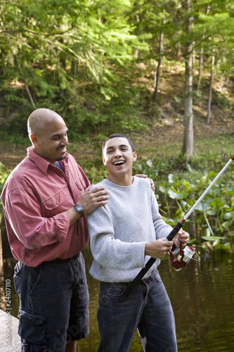Hispanic teenager and father fishing in pond