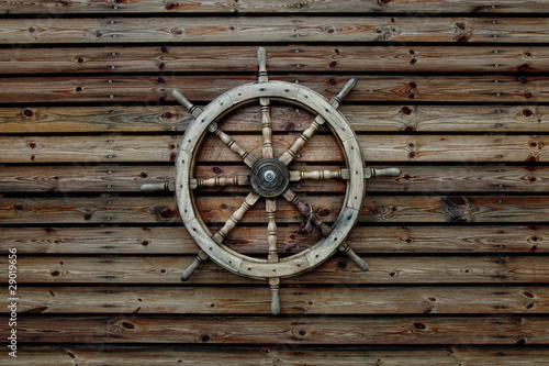 Steering wheel of the ship on a wooden wall