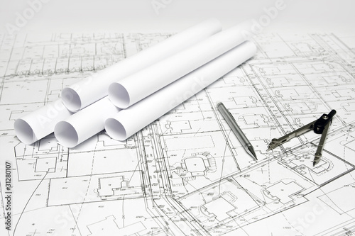 cyrkiel i ołówek na białym planie architektonicznym obok rulonów