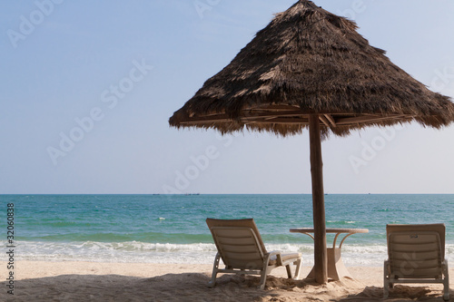 Соломенный зонт и лежаки на пустынном пляже
