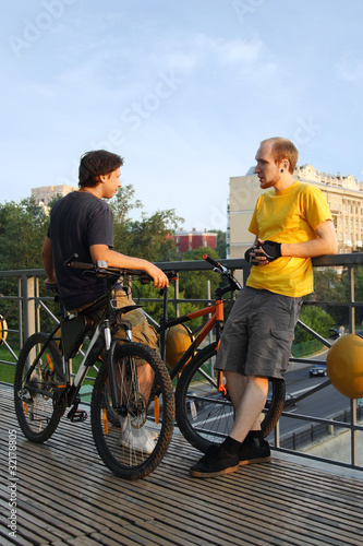 two young men in sport clothes standing on bridge near bicycles
