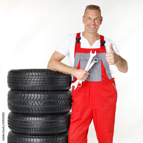 Motor mechanic next to a set of winter tyres shows thumb up