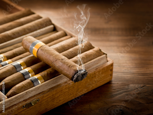 smoking cuban cigar over box on wood background