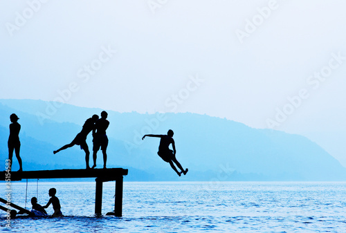 Silhouettes of kids who jump off dock on the lake