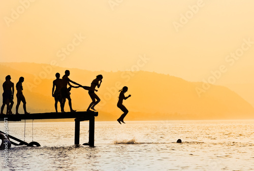 kids jumping off dock at sunset