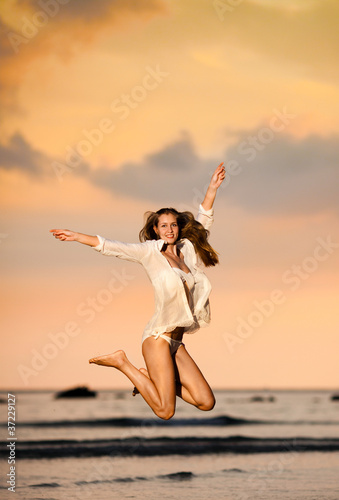 Beautiful young woman jumping on a beach at sunset