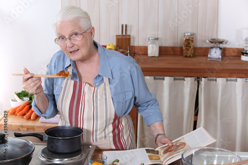 Elderly woman cooking dinner with the help of a recipe