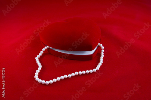 Cofanetto cuore rosso e collana di perle su fondo rosso