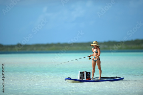 Woman in bikini fishing and paddle boarding
