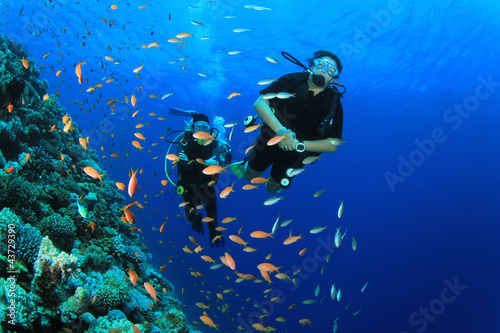 Female Scuba Divers swim through tropical fish on ocean reef