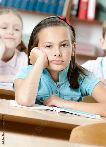Sad beautiful schoolgirl sits at the desk and leans on her hand