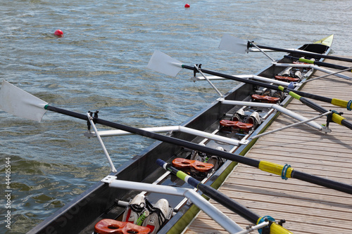 Long sport boat with oars stands at wooden pier at sunny day.