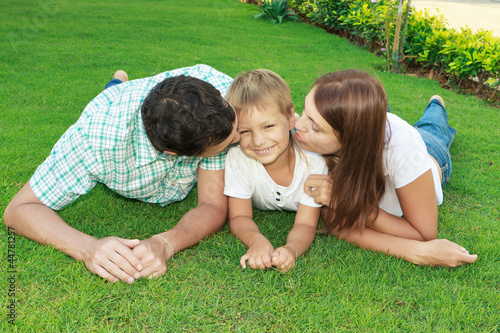 Родители целуют сына лежа на траве