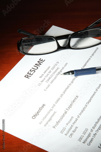 Closeup of resume with glasses and pen on wooden table
