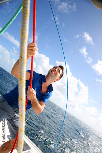 Young man lifting the sail of catamaran during cruising