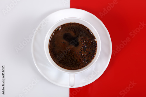 Kawa w białej filiżance na biało czerwonym tle, widok z góry.