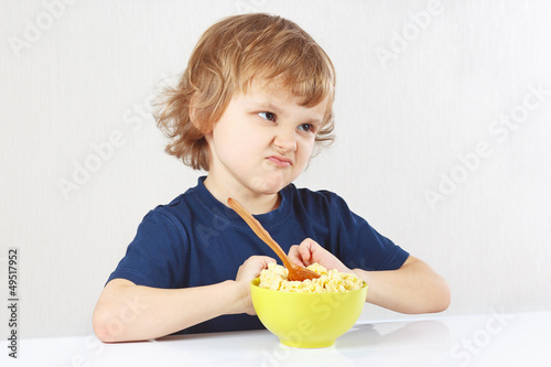 Little cute blonde boy refuses to eat a porridge