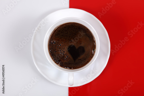 Kawa w białej filiżance z sercem, na biało czerwonym tle.