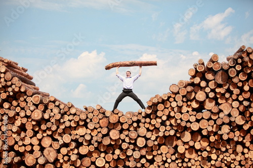 man on top of large pile of logs, shouting, lifting heavy log