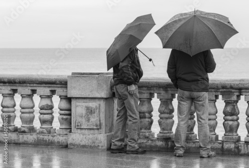 Hombres con paraguas apoyados en balustrada
