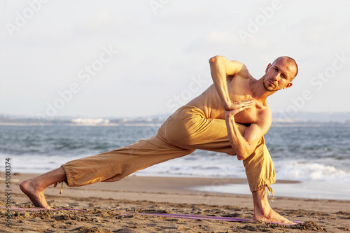 Bare-chested man practicing yoga on mat at beach