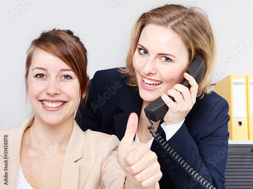 Two business women work in the office, show thumb up