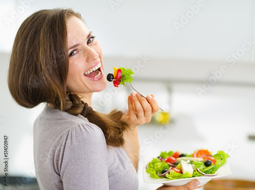 Smiling young woman eating fresh salad in modern kitchen