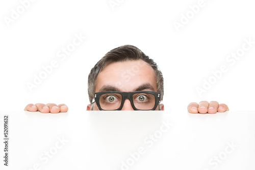 Funny nerd peeking from behind the desk isolated on white