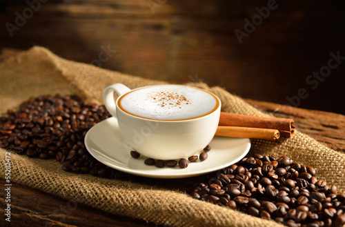 A cup of cappuccino and coffee beans on old wooden background