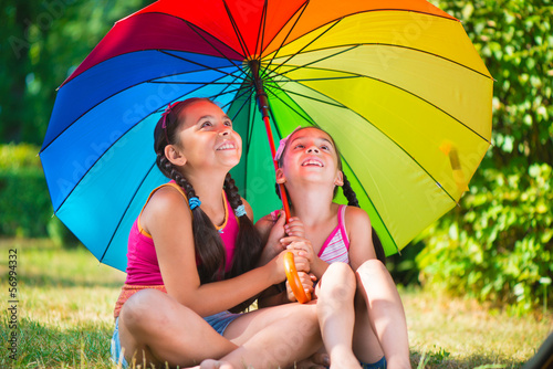 Happy sisters under colorful umbrella in park