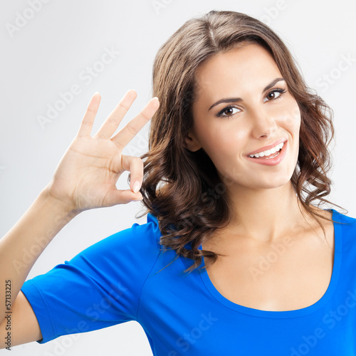 Young woman showing okay gesture, over grey