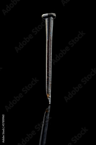 A Nail Photographed on a Black Background With Reflection