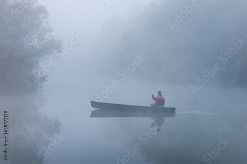 Man rowing in a boat on foggy morning